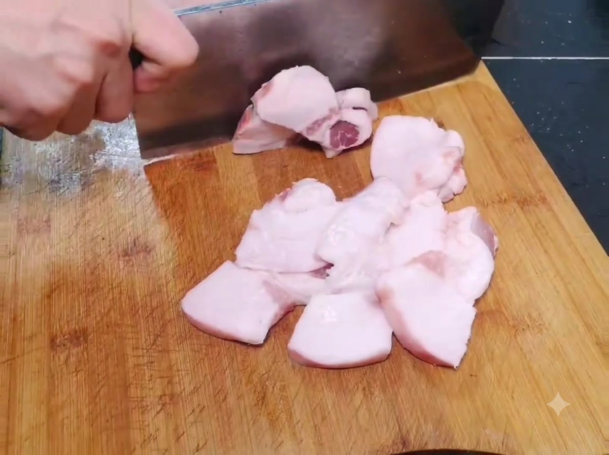 木製のまな板の上で、薄く幅の広い生の豚肉のスライスを切っている様子。