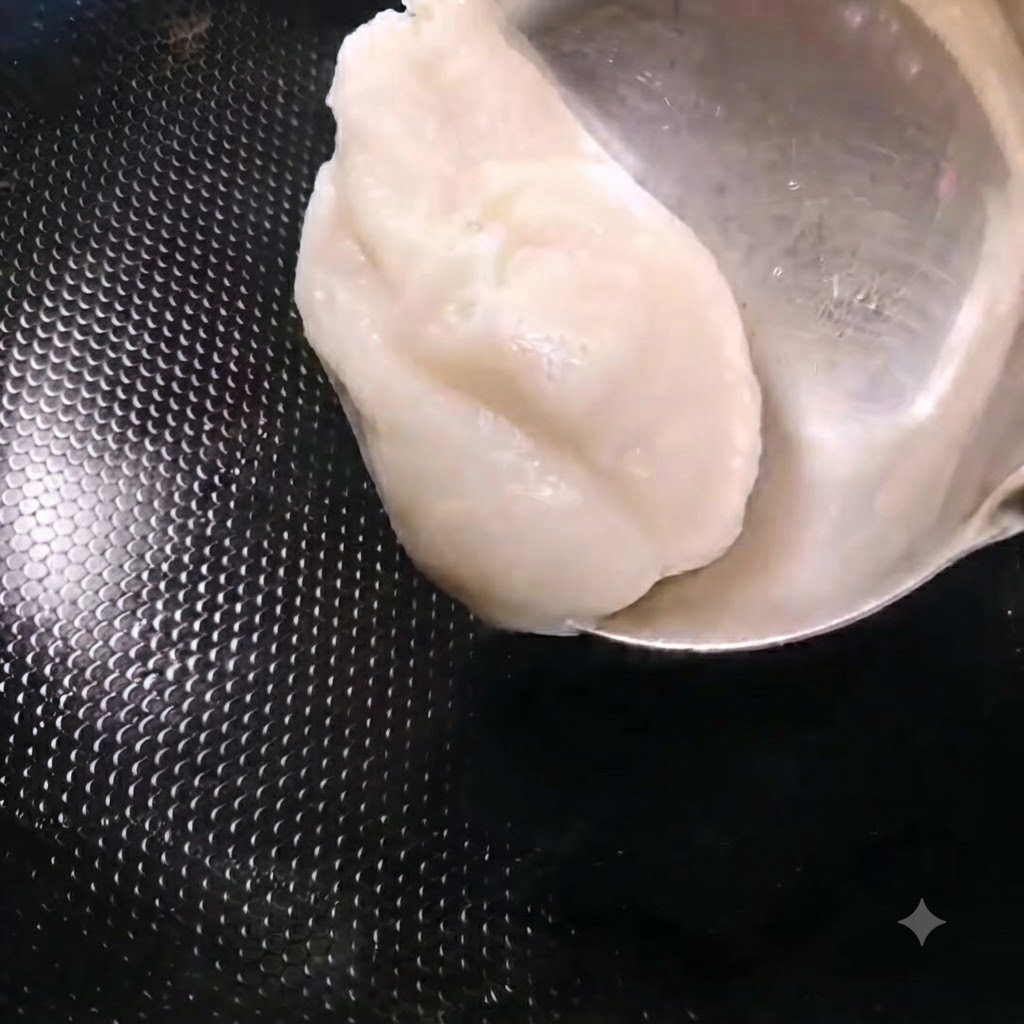 金属製のお玉を使って、熱した黒い中華鍋に白い豚ラードをすくい入れている様子。