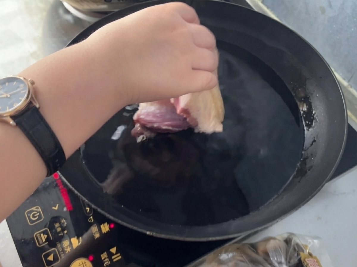 生姜と料理酒を入れた冷水の鍋に、手が豚肉の塊を入れようとしている様子。