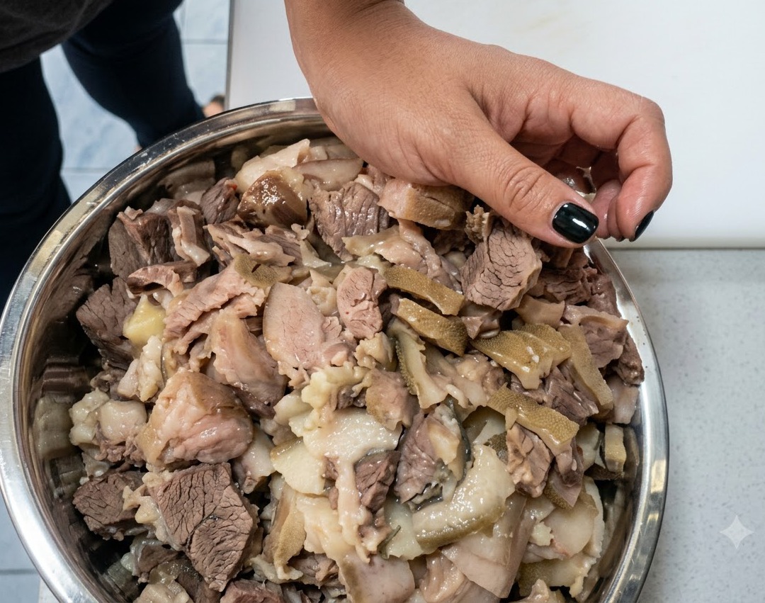 大きなスチール製ボウルの中で、カットされた豚肉の塊の上に高度数の白酒が注がれている様子。