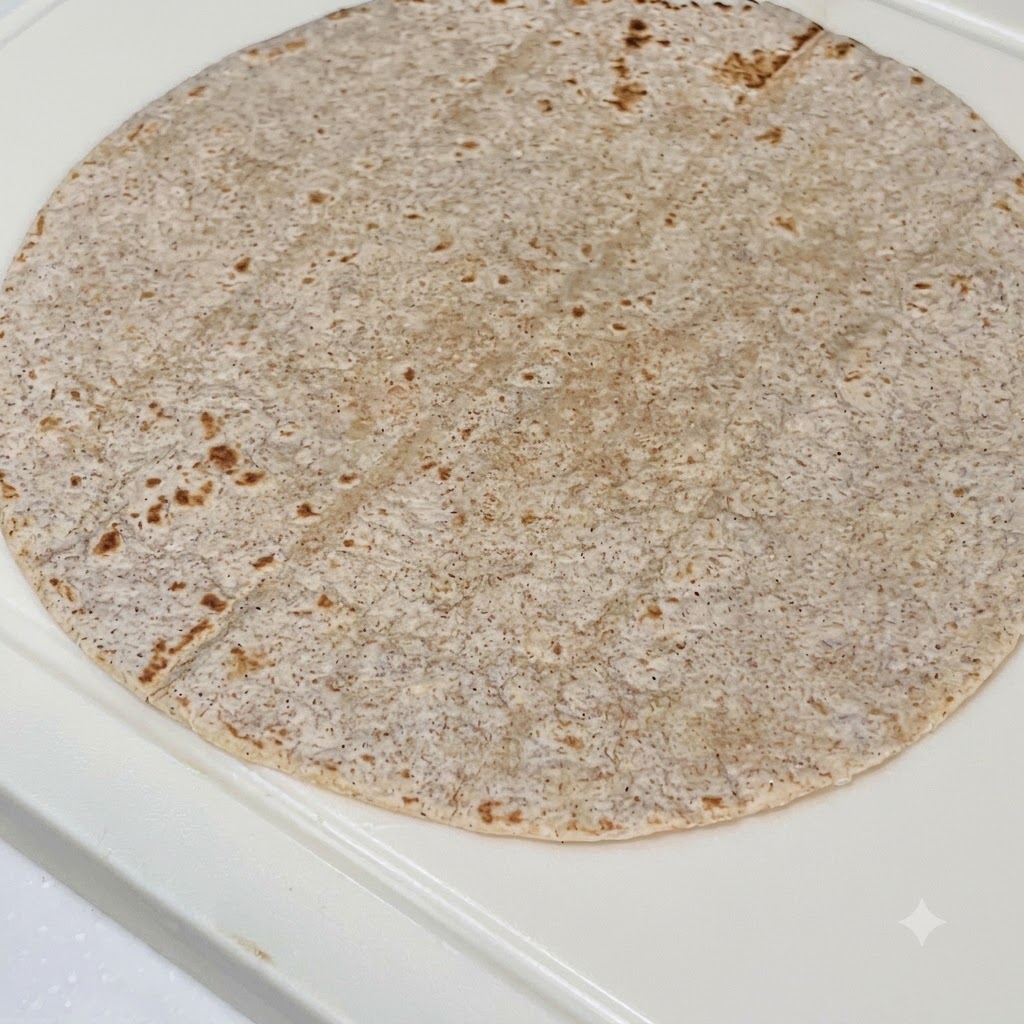 全粒粉トルティーヤの上に、ピーナッツバターソース、スライスしたチキン、紫キャベツ、フレッシュレタスを重ねている様子。