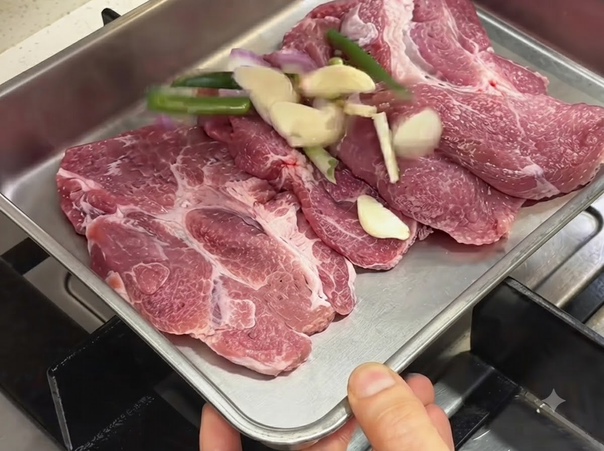金属製のトレイに並べられた生の豚肉と、スライスしたニンニク、青ネギ、シャロット。