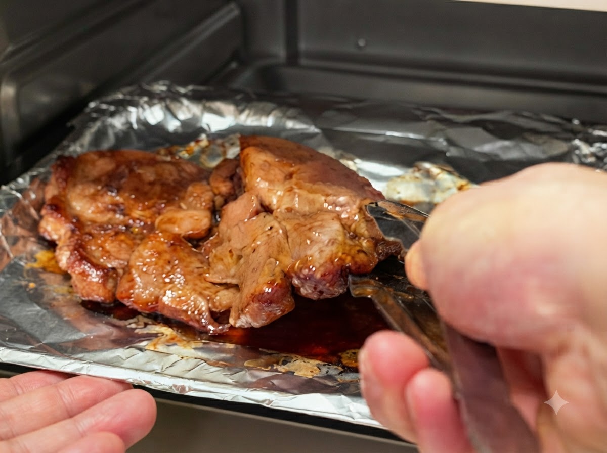 金属製のキッチン用トングを使って、ベーキングトレイの上で豚肉を裏返している様子。