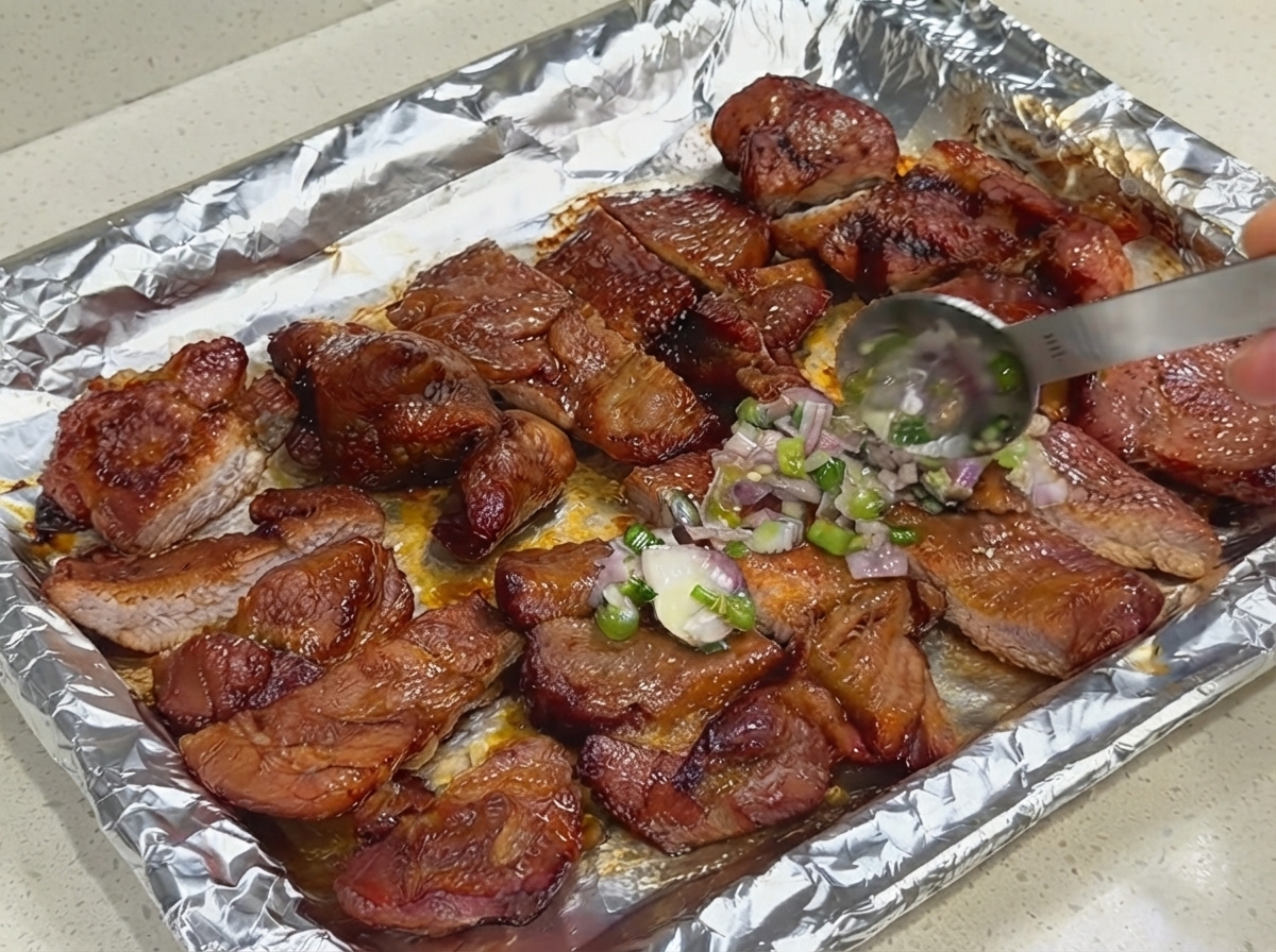 ホイルを敷いたベーキングシート上のスライスした豚肉に、スプーンを使って特製ネギ・シャロットソースを塗っている様子。