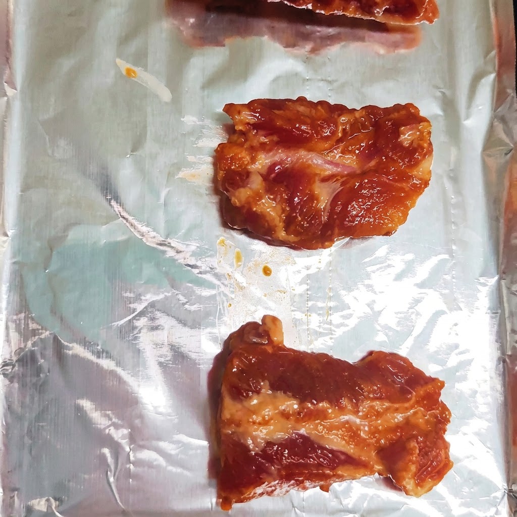 アルミホイルを敷いた天板の上に、下味をつけた豚スペアリブがきれいに1列ずつ並べられています。
