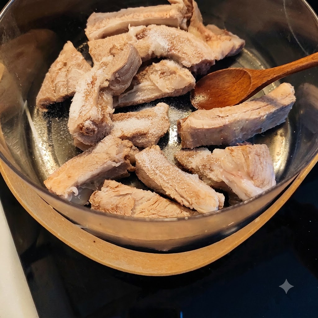 塩や調味料がふりかけられた下茹で済みの豚スペアリブの上に木製のスプーンが置かれている様子。