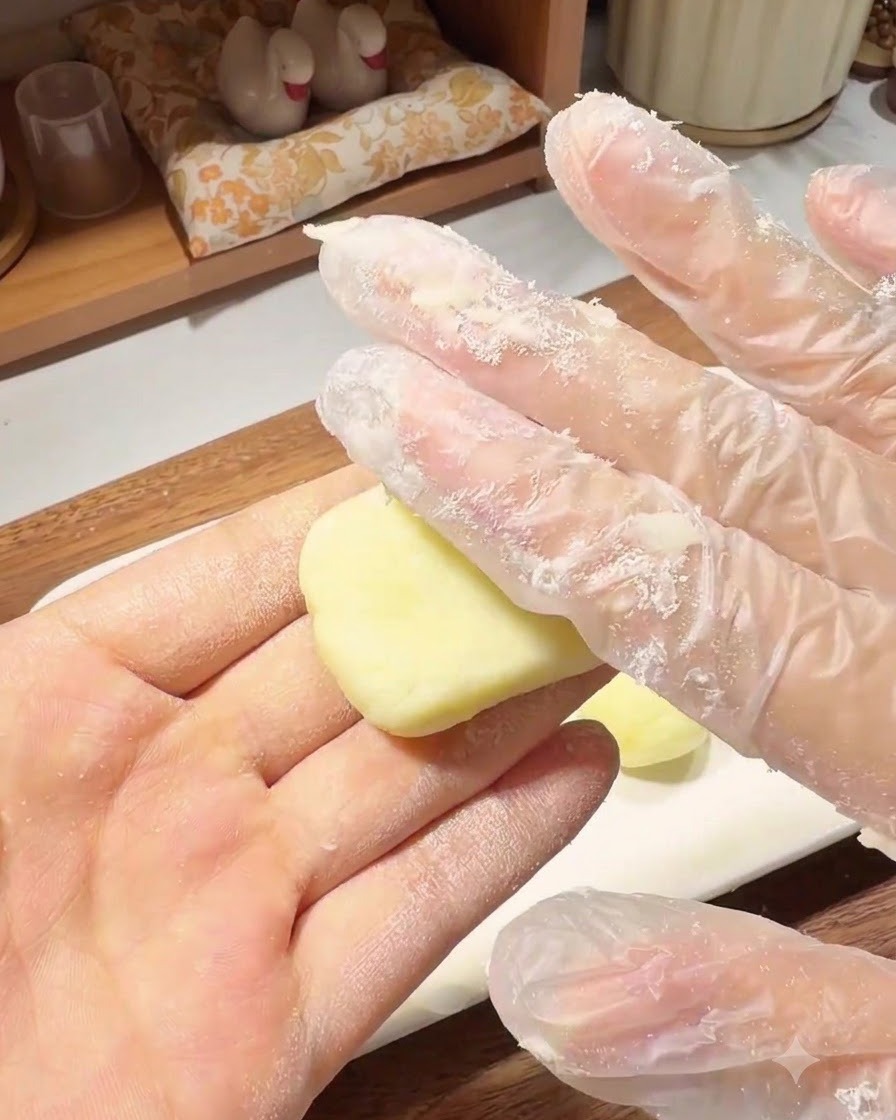 手袋をはいた手が、丸めたポテト生地を手のひらで平らな丸いパンケーキ状に押さえている様子