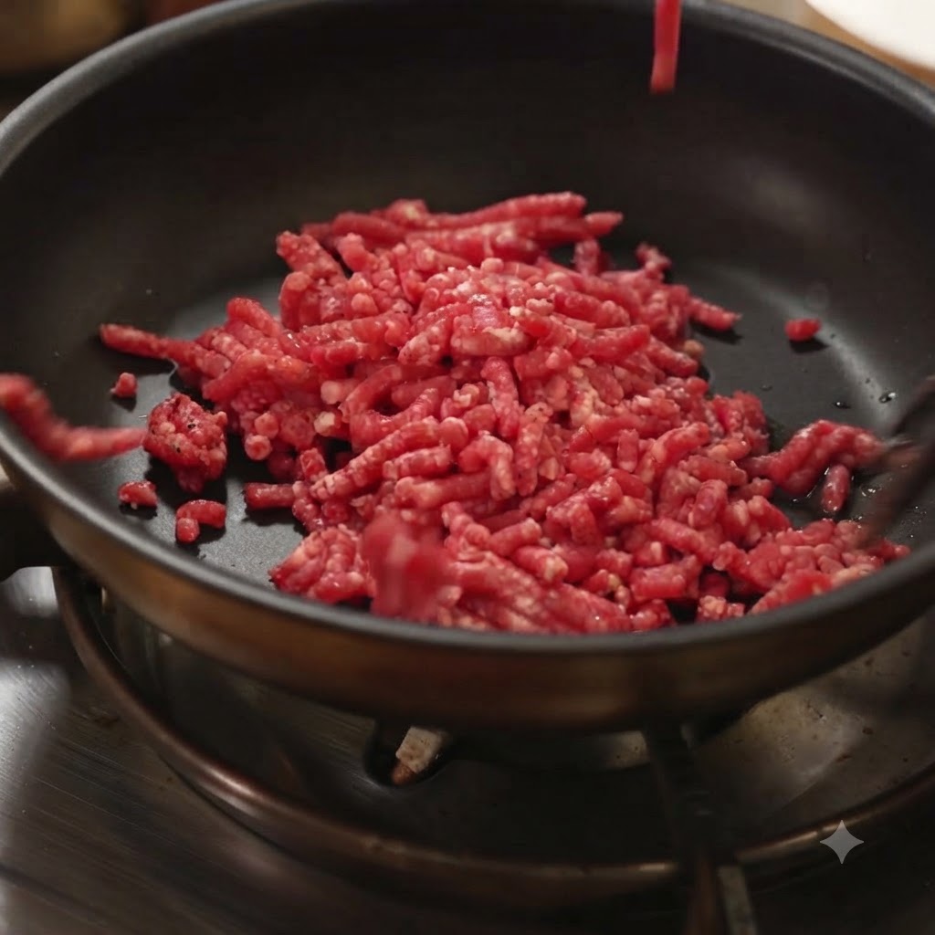 熱した黒いフライパンに生のひき肉が投入されている様子。