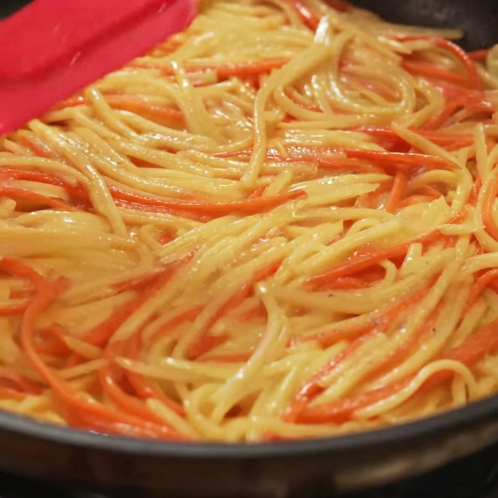 フライパンの中で、スパチュラを使ってポテトと人参の生地を均一に広げ、平らにしている様子。