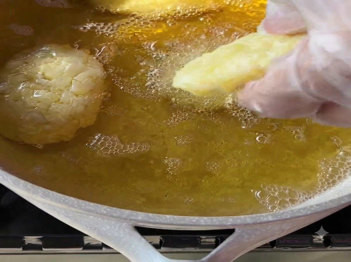 手袋をした手が、熱して泡立つ調理油の入ったフライパンに成形したポテトパティをそっと入れている様子。