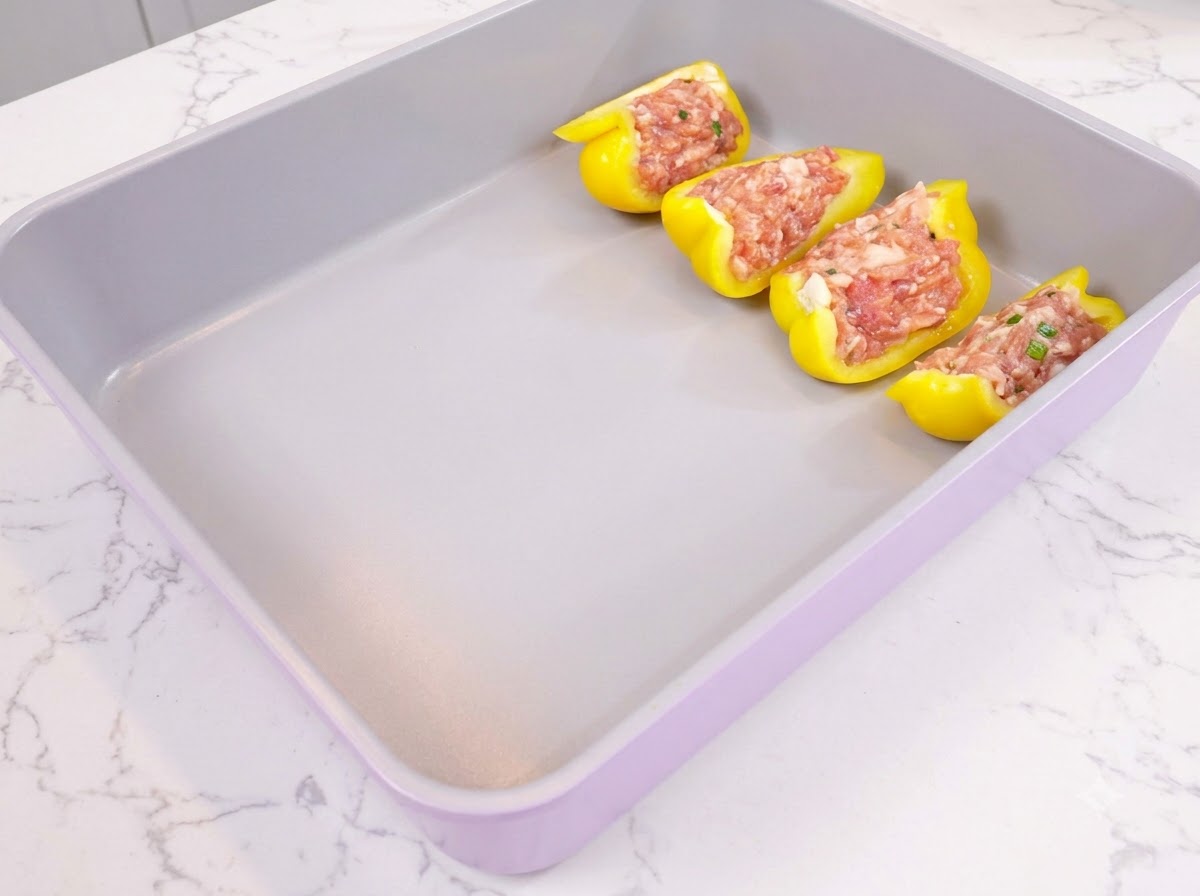 特製のひき肉が詰められた黄色いピーマンの半身が、紫色の耐熱皿にきれいに並べられている様子。