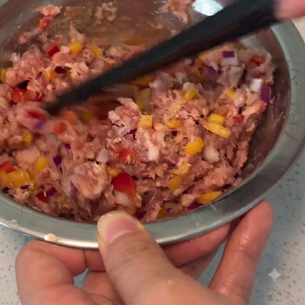 金属製のボウルの中で、箸を使って豚ひき肉、野菜、調味料を一緒に混ぜ合わせている様子。