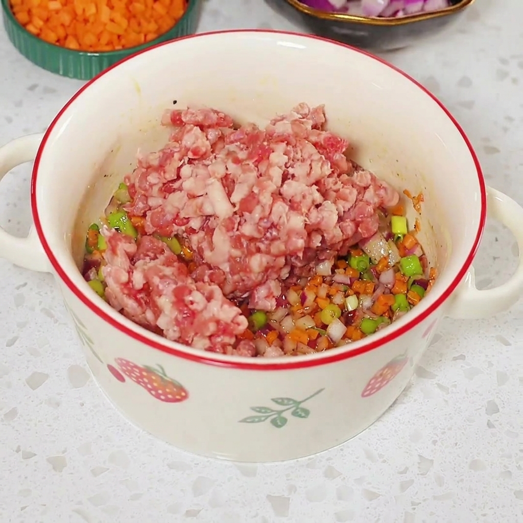 白いボウルの中の味付けされた野菜の上に、生ひき肉がのせられている様子。