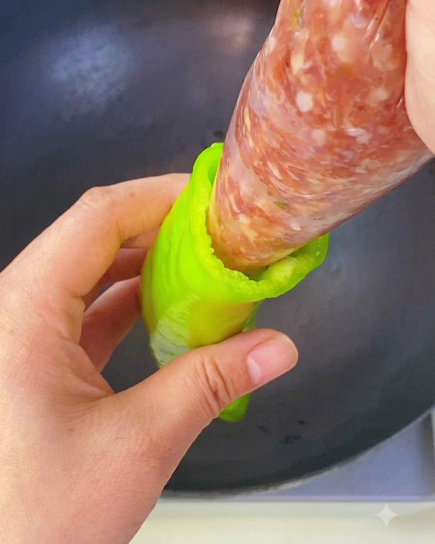 絞り袋に入れた味付け肉ダネを、緑色のピーマンの空洞へ直接絞り込んでいる手の様子。