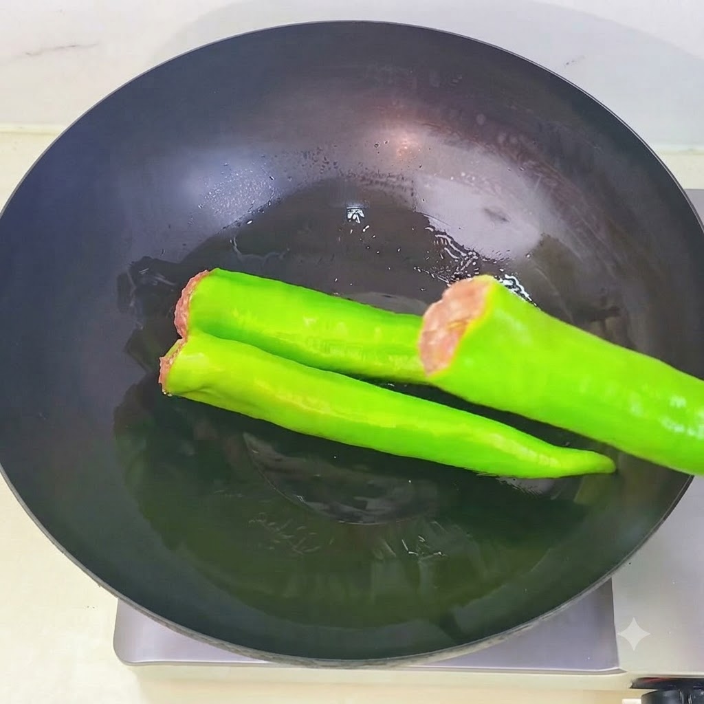 油を熱した中華鍋の中に、肉詰めしたピーマンを順番にきれいに並べている様子。