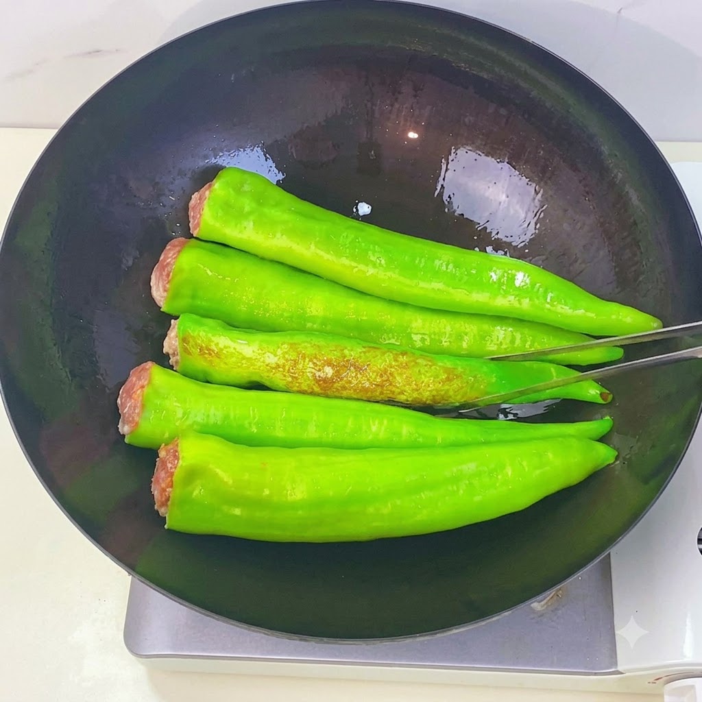 中華鍋の中で焼かれている緑色のピーマンが、トングで裏返され、茶色い虎皮状の焼き目を見せている様子。