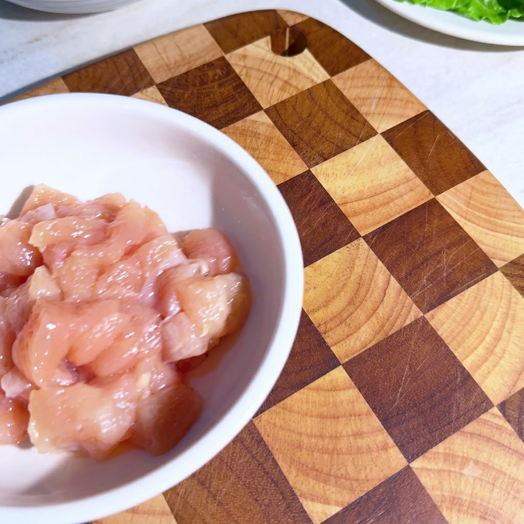 白いボウルに入った小さく切った鶏肉。混ぜ合わせる前に計量したスパイスが上にかかっている様子。