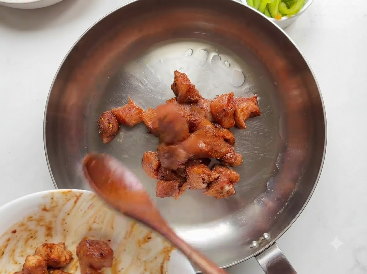 ステンレス製のスキレットでマリネした鶏肉の塊が調理され、焼き色がついている様子。