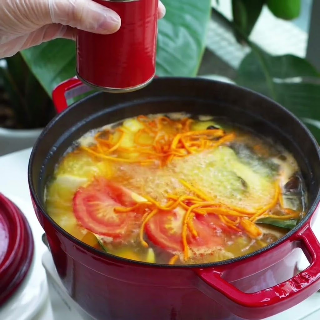 スプーン一杯の赤いペースト状の調味料が沸騰する野菜スープの鍋に加えられている様子。