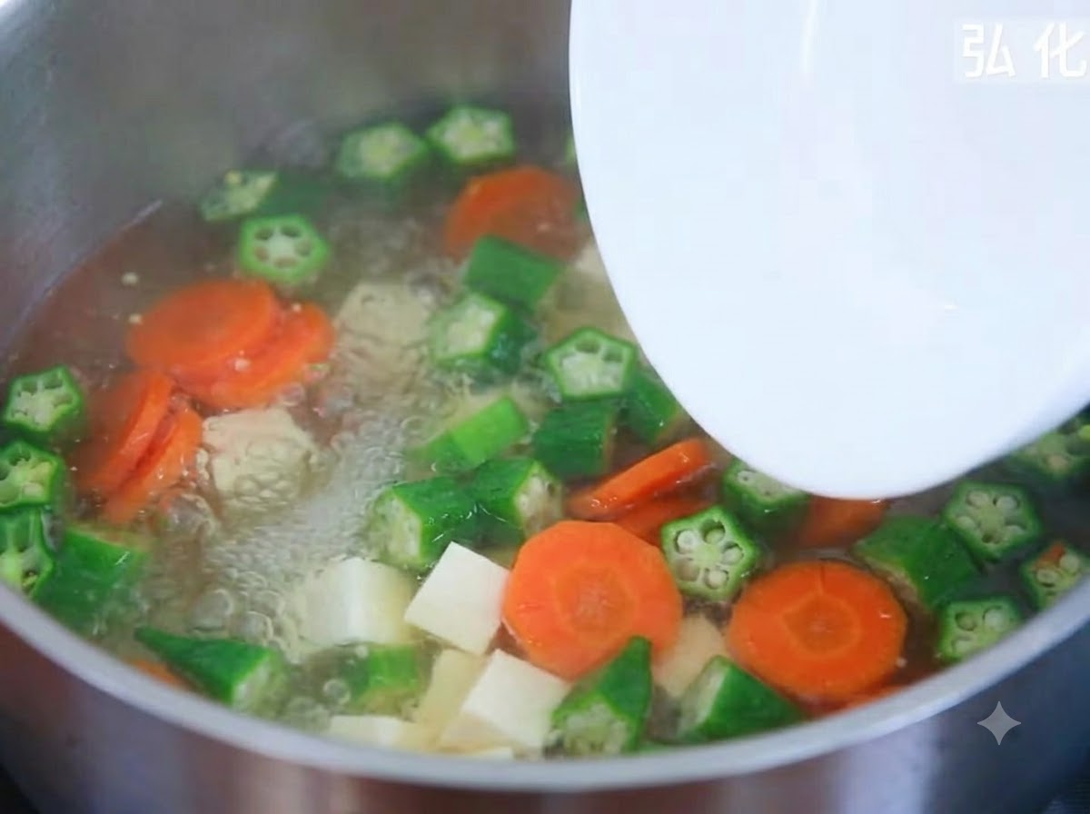 皿から絹豆腐のサイコロを沸騰中の野菜スープの鍋に加えているところ。
