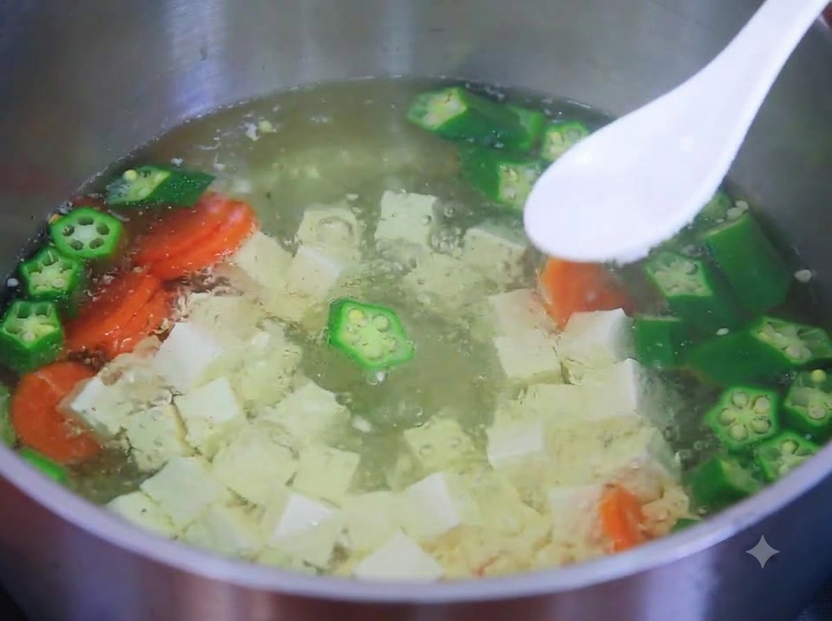 白いスプーンに塩をのせ、豆腐、オクラ、ニンジンのスープの鍋の上にかざしているところ。