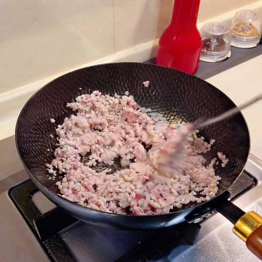刻みネギとみじん切りニンニクが中華鍋のひき肉と一緒に炒められている様子。