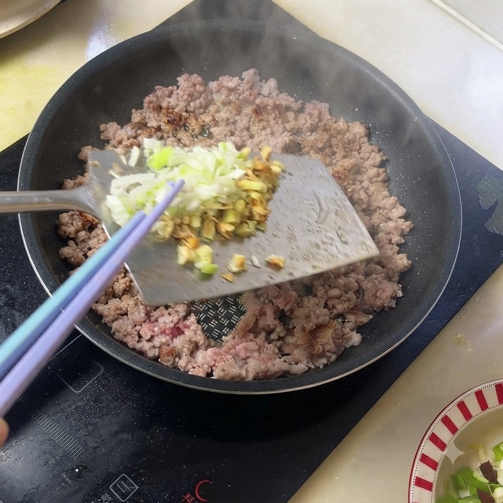 調理中の豚ひき肉に刻みネギと生姜を加えている様子。
