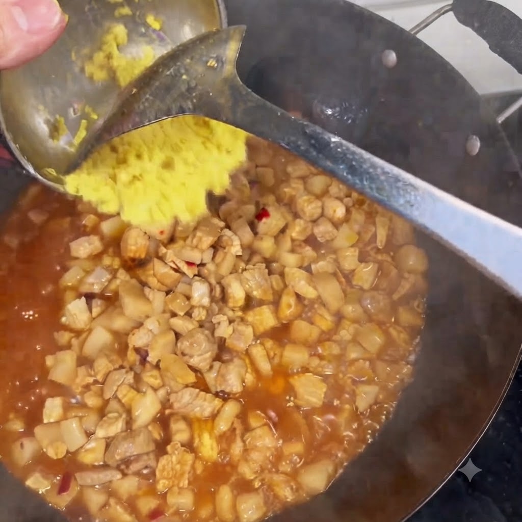 煮込んでいる肉とソースが入った中華鍋に、お玉から刻み生姜を加えている様子。