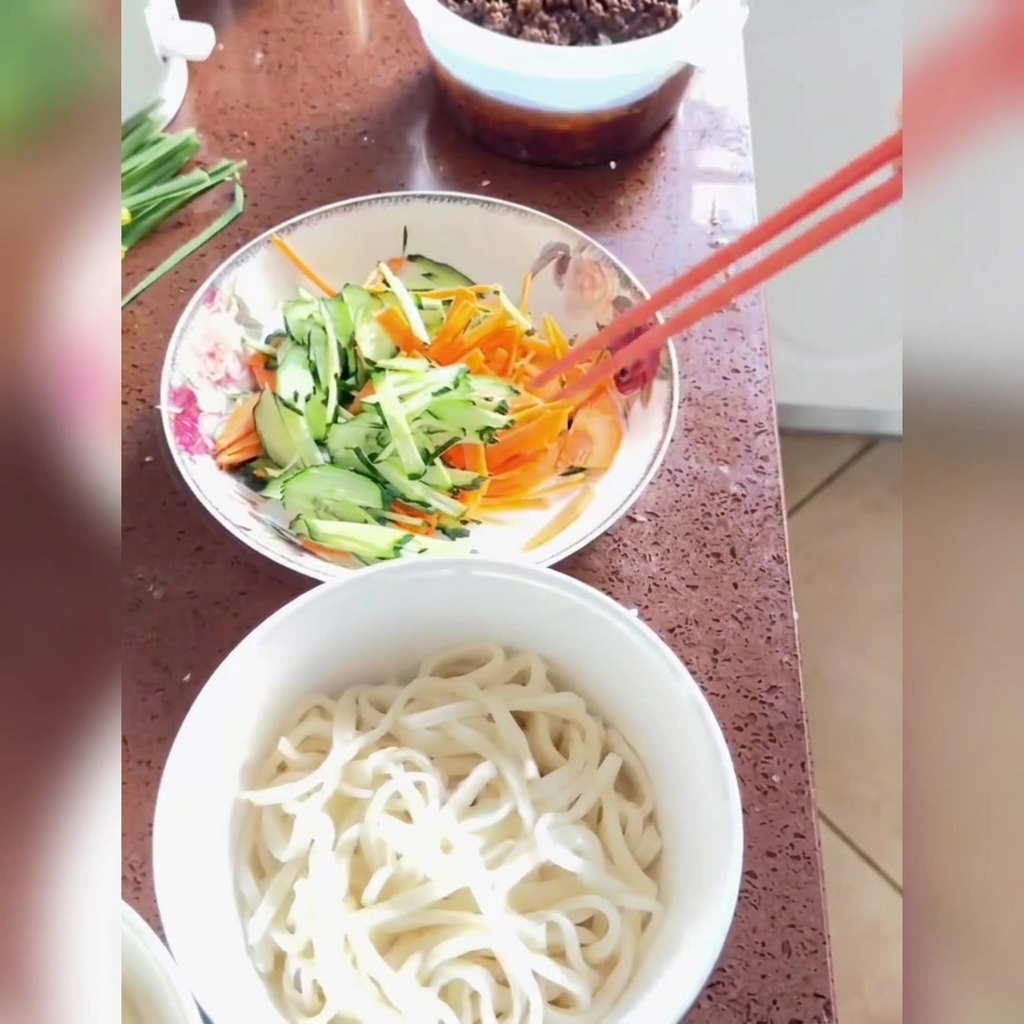 白い丼に盛り付けられた麺の上に、千切りきゅうりと人参、そして特製の肉味噌ソースが美しくかけられている様子。