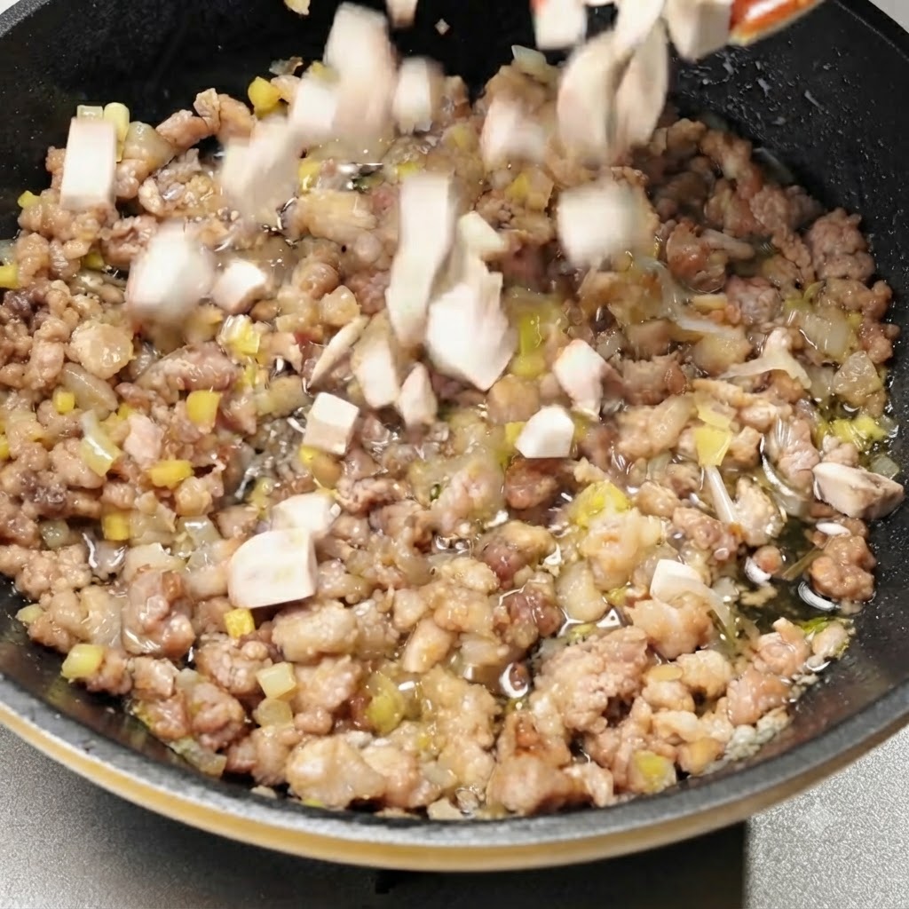 味付けされた豚肉の入ったフライパンに、角切りマッシュルームを投入している様子。