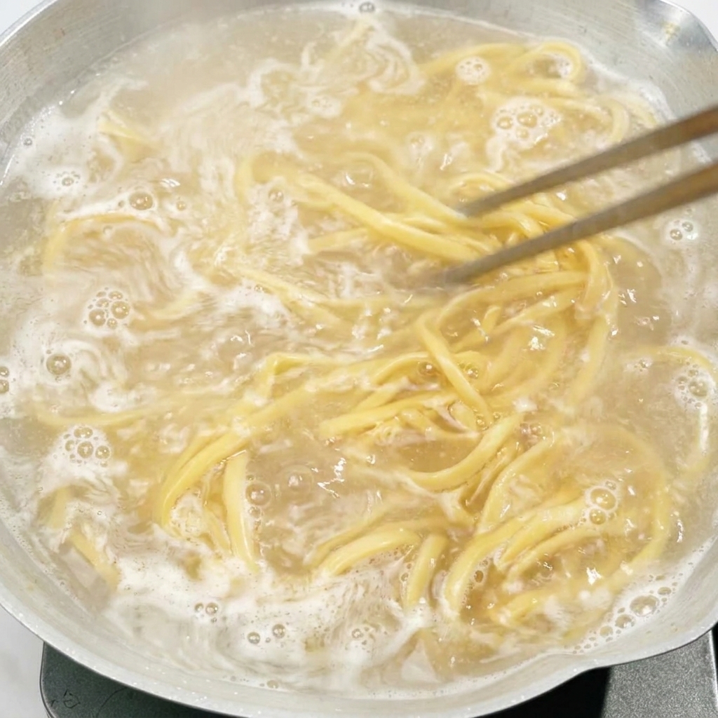 お湯の入った鍋の中で、箸を使って麺をかき混ぜている様子。