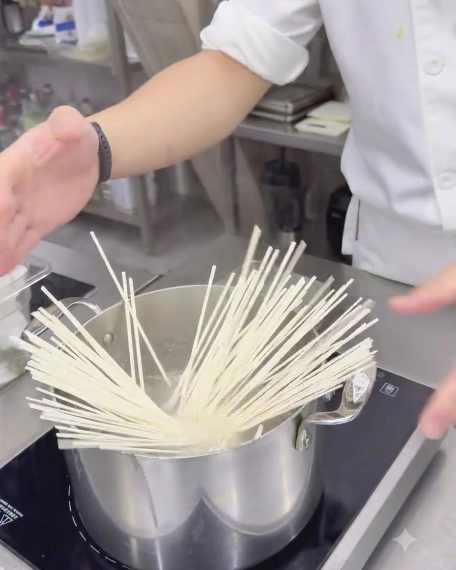 ステンレス製の鍋の沸騰したお湯に投入される乾燥うどん。