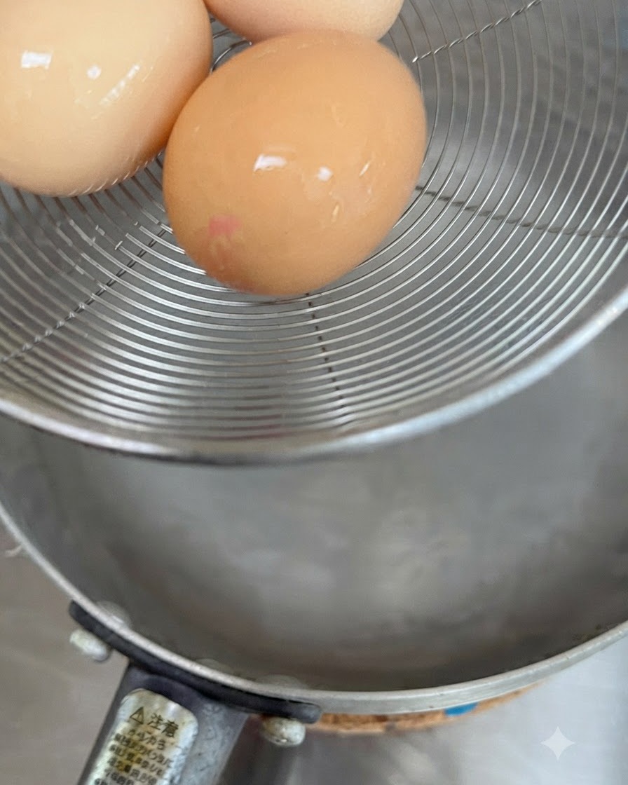 お湯の入った鍋に、生卵3つを網じゃくしに乗せて入れている様子