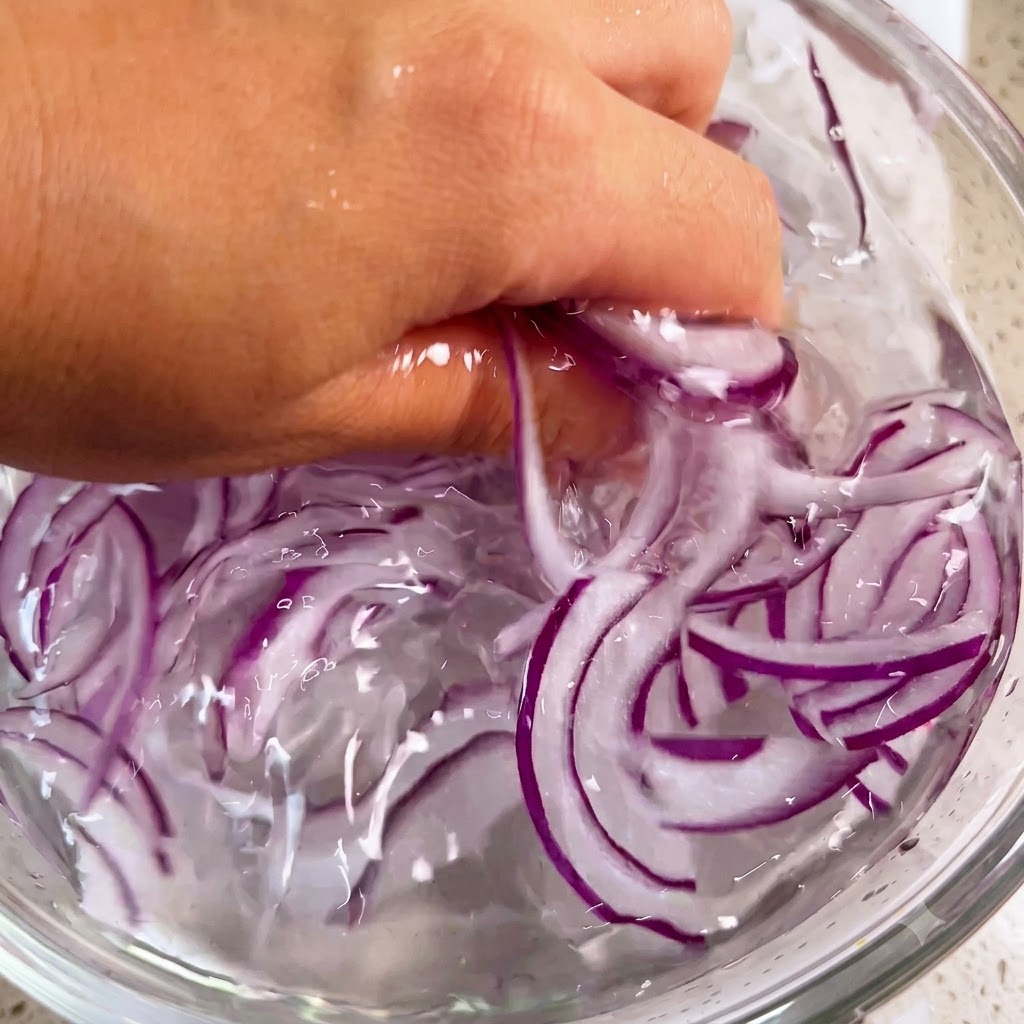 氷水が入ったボウルの中で、手で優しく紫玉ねぎを洗っている様子。