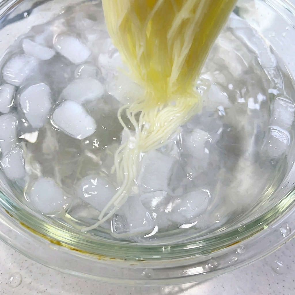 氷が入った氷水の中で、茹で上がったそうめんを箸でかき混ぜている様子。