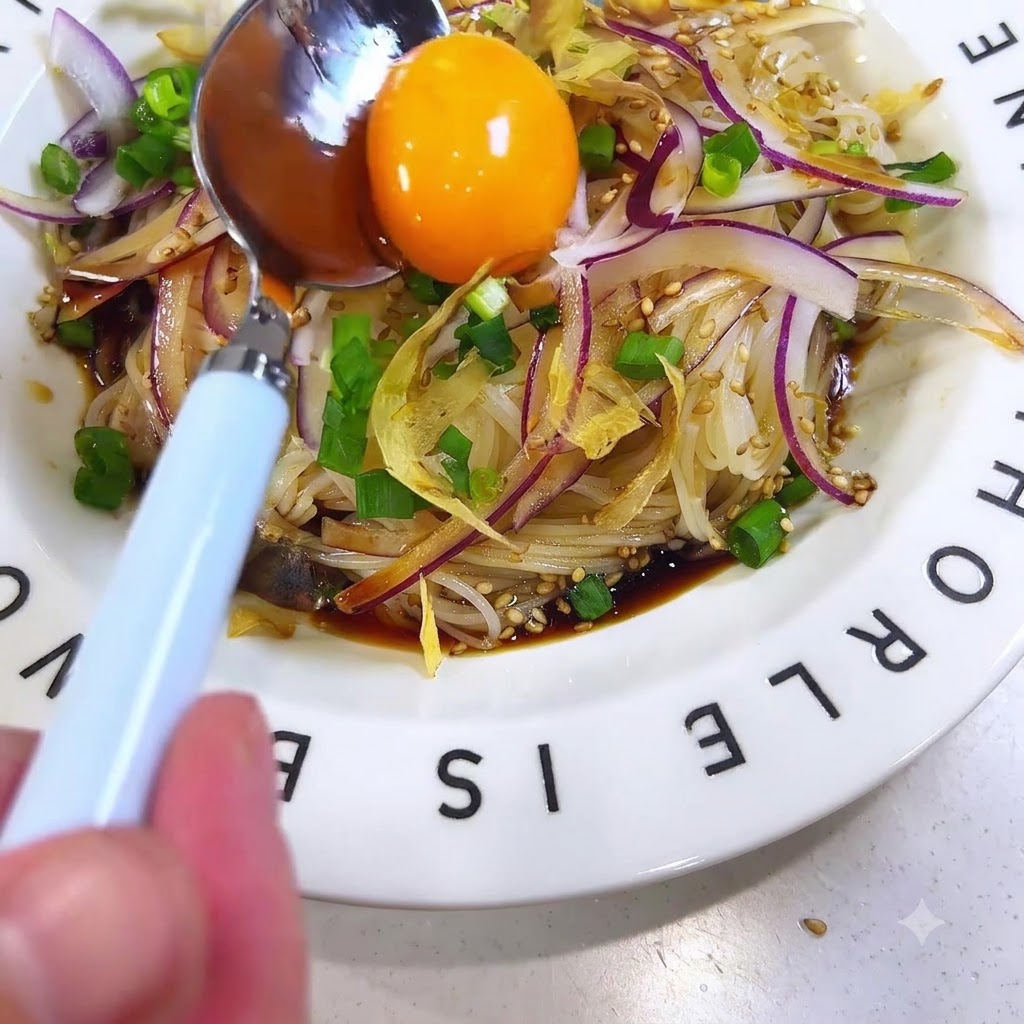 トッピングされたそうめんの中央に、スプーンを使って鮮やかな生の卵黄をのせている様子。