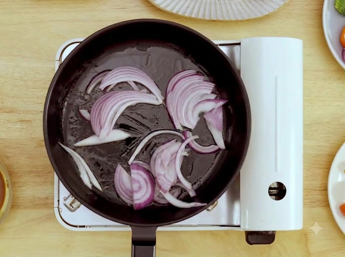 熱したフライパンの中で、木べらを使いスライスした赤玉ねぎを炒めているところ。