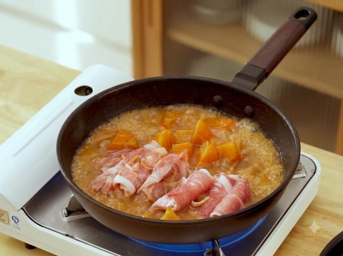 茶色く泡立つ味噌の煮汁とニンジンの入ったフライパンの中に、丸められた生の牛肉スライスが並んでいるところ。