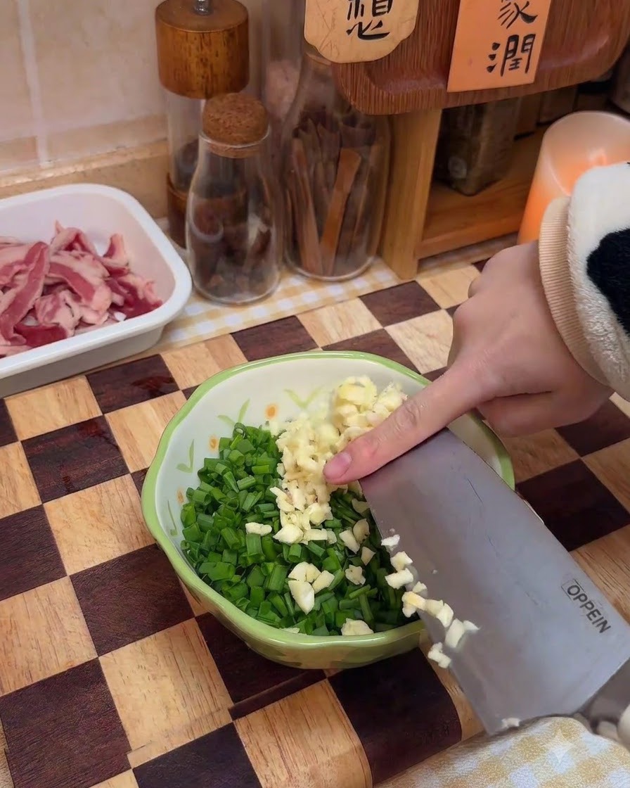 刻んだ青ねぎやスパイスの入ったボウルに、みじん切りにしたニンニクを加えている様子