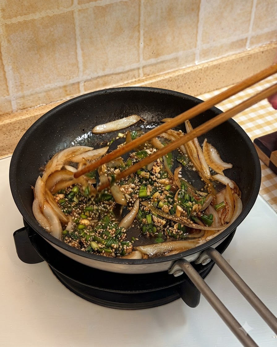 調理済みの牛肉をフライパンに戻し、玉ねぎやたれと一緒に箸で絡めている様子
