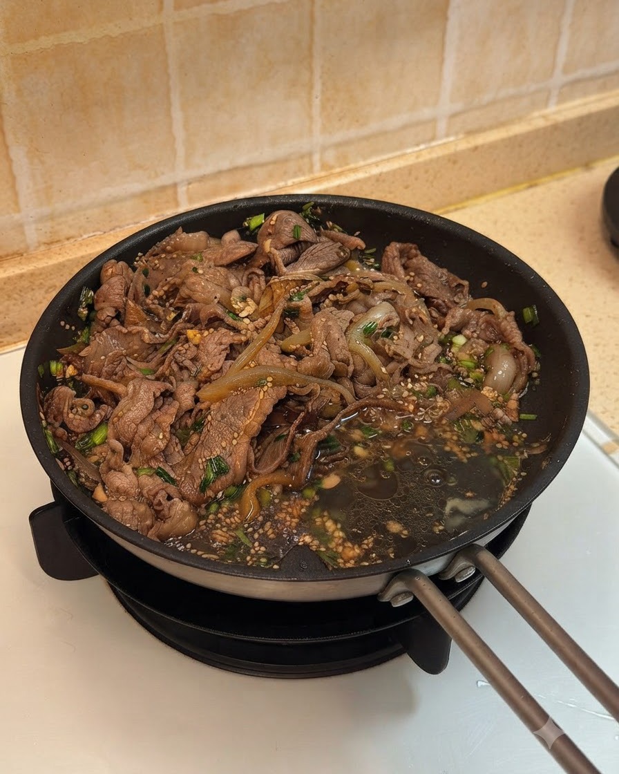 たれが絡まった牛肉と玉ねぎの横で、フライパンに卵を2個割り入れている様子