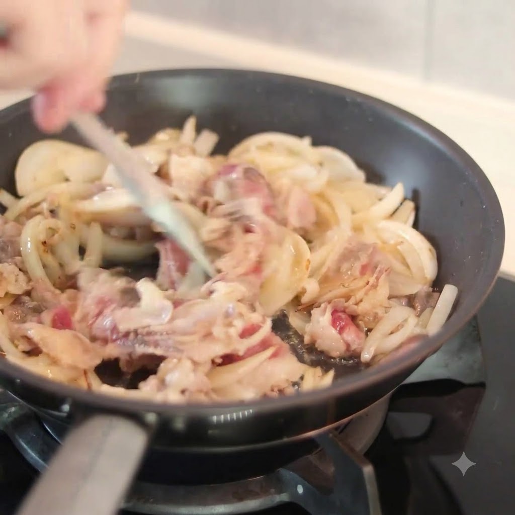 熱いフライパンの中の牛肉と玉ねぎの上から黒っぽいソースをかけ、ヘラで混ぜ合わせている様子。
