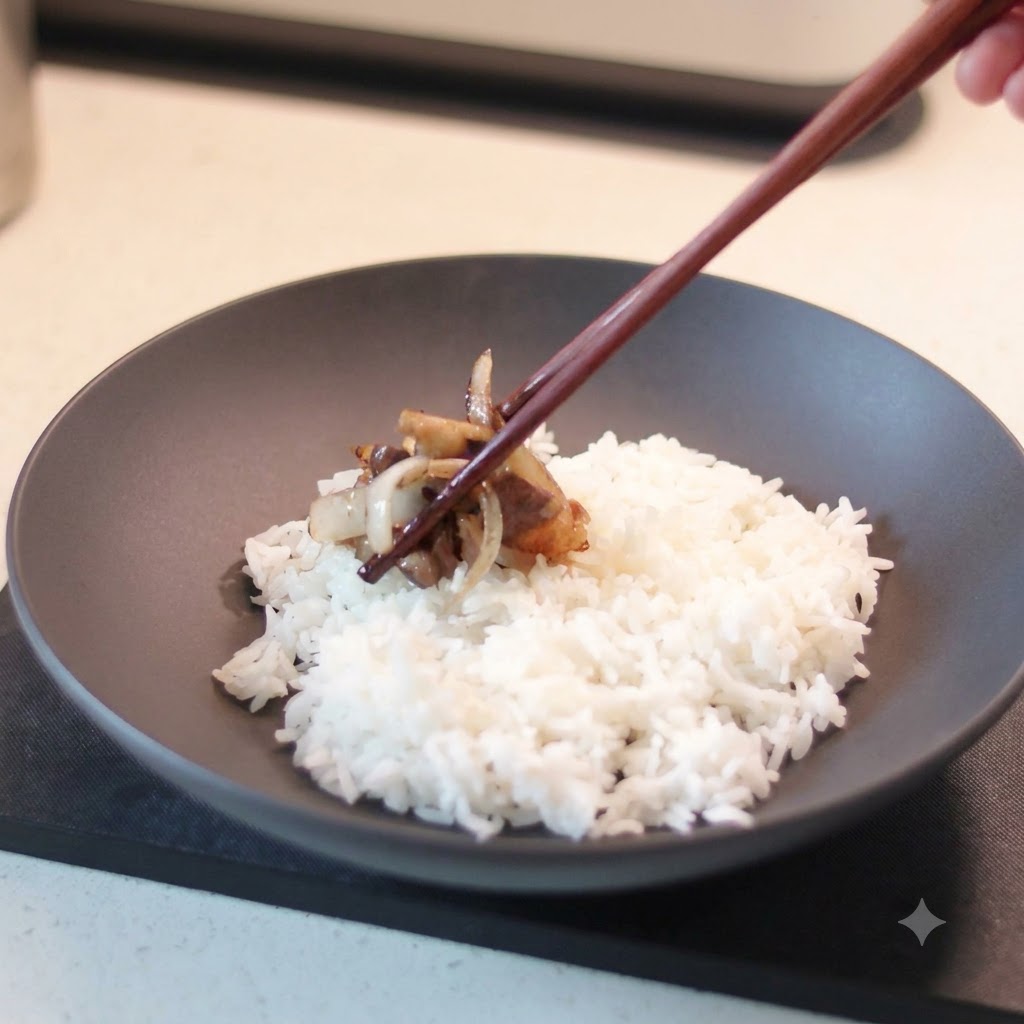 箸を使って調理したての牛肉と玉ねぎをつかみ、白いご飯が入った黒い陶器の丼にのせている様子。