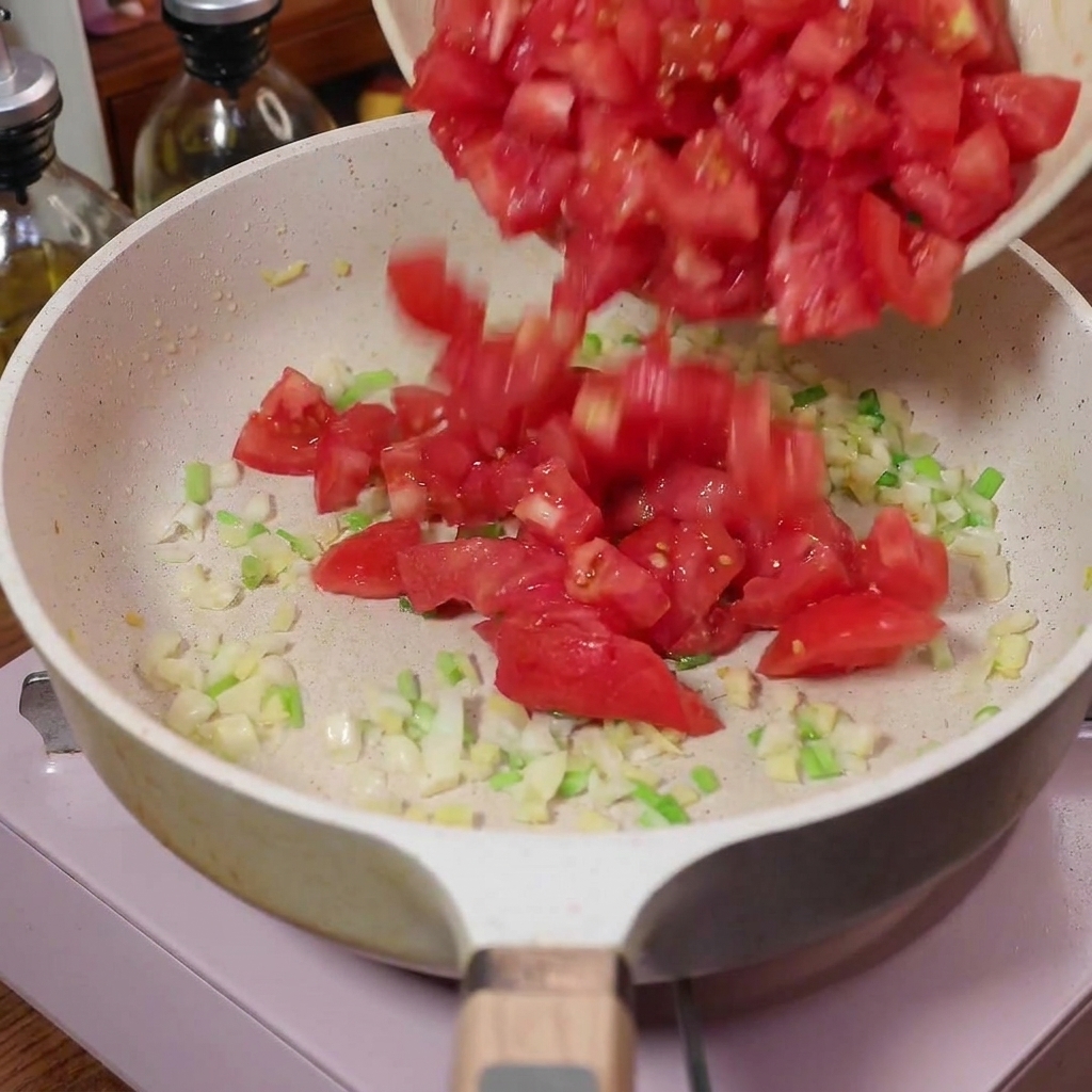 炒めた香味野菜が入ったフライパンに、角切りトマトが投入されている瞬間。