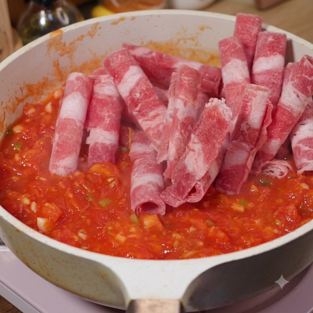 柔らかくなったトマトが入ったフライパンに、薄切りの牛肉が加えられて一緒に炒められている様子。