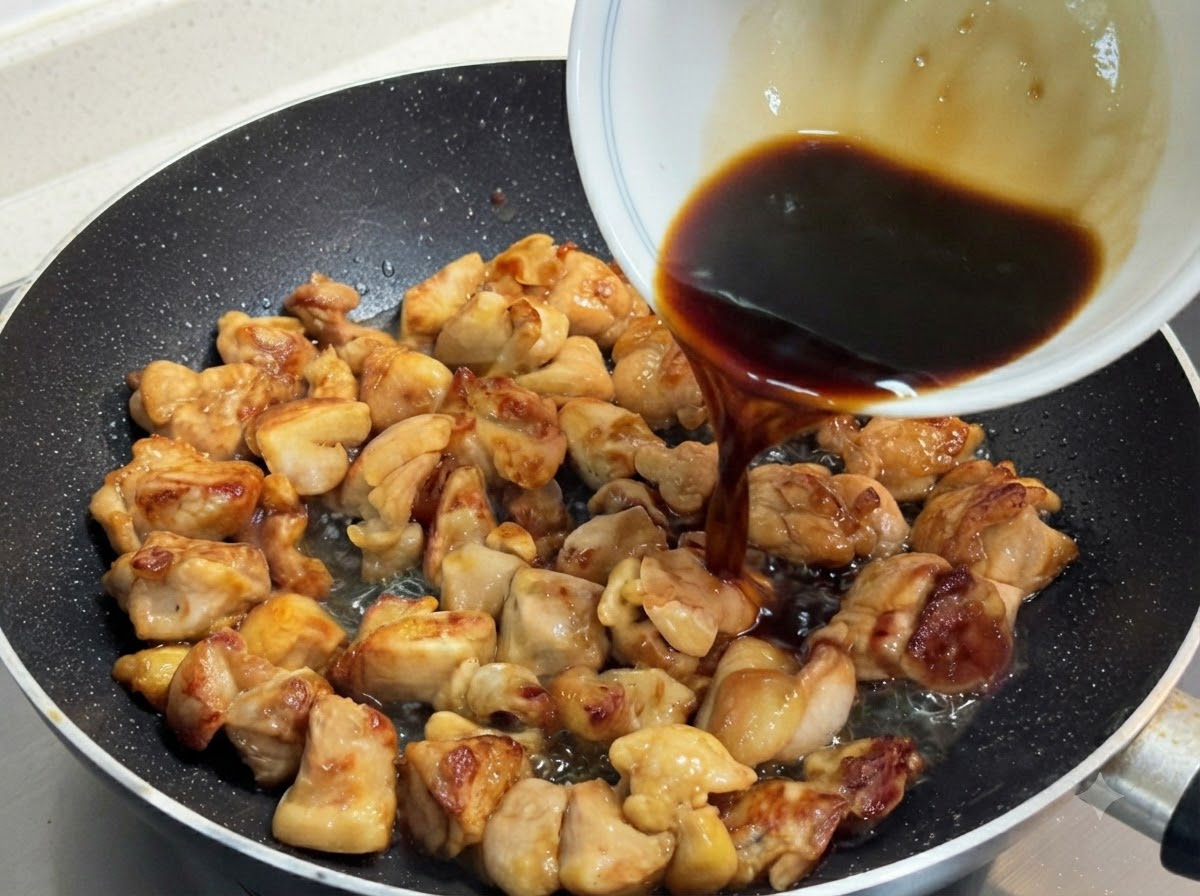 きつね色に焼けた鶏肉が入ったスキレットに、白いボウルから濃い色の合わせダレを注いでいる様子。