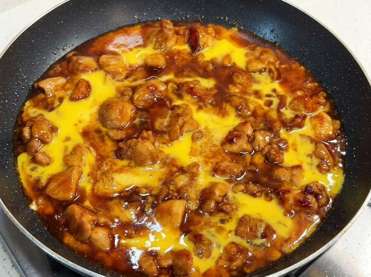 鶏肉と濃厚なタレが入ったフライパンに、生卵の液が上からかかっており、蓋がされている様子。
