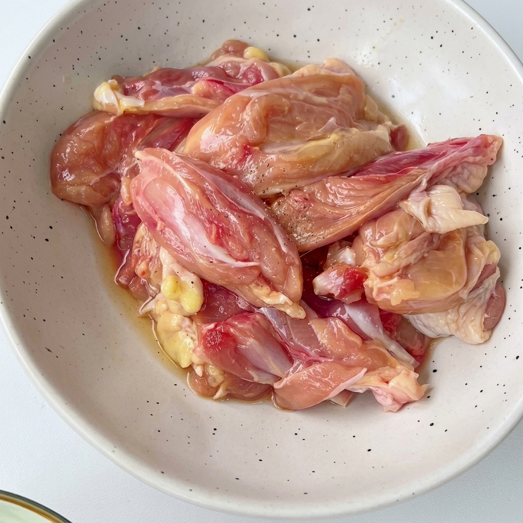 白い斑点模様のボウルの中で、切り分けた鶏肉に調味料や香味野菜がしっかりと混ぜ合わせられている様子。