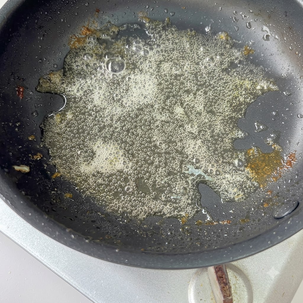 残りの油が入った熱いフライパンの中で、スライスした赤玉ねぎが炒められている様子。