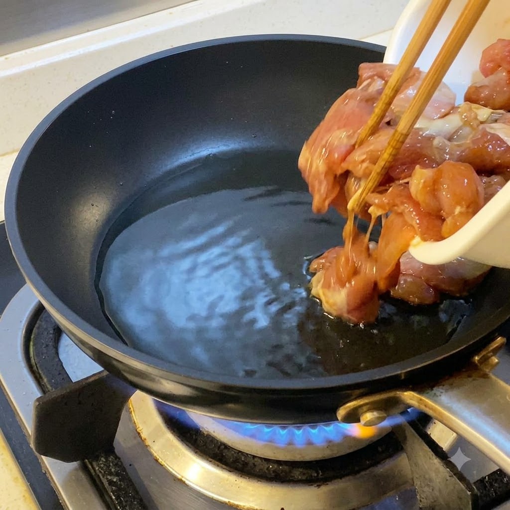 油を引いた熱したフライパンに、菜箸を使って下味をつけた鶏肉を入れている様子。